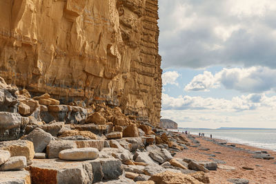 People walks on golden beach underneath cliffs.  jurassic coastline of west bay in dorset. uk