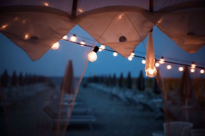 Close-up of illuminated lighting equipment hanging against sky at sunset