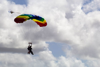 Low angle view of men paragliding against sky