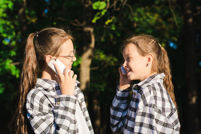 Two cheerful girls talking on dump phones in a sunny summer park