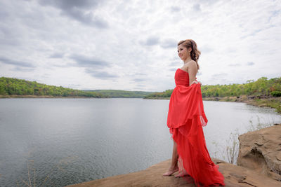 Woman in red dress standing at lakeshore