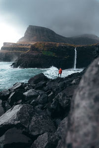 Rear view of man standing on rocks by lake against mountains