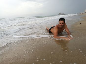 Man lying on shore at beach against sky