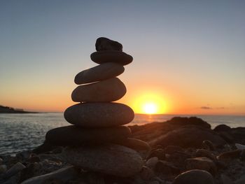 Stack of pebbles on beach against sky during sunset