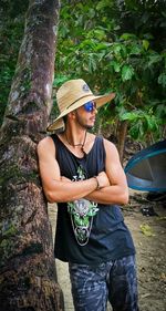 Young man wearing sunglasses standing on tree trunk against plants