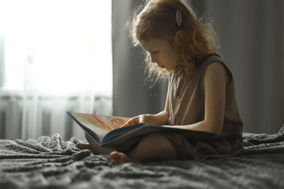 Girl reading book sitting on bed at home