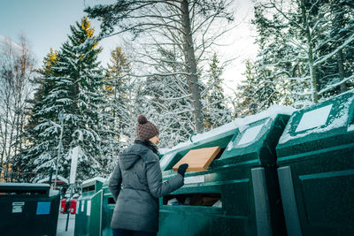 Woman putting cardboard box in garbage can during winter