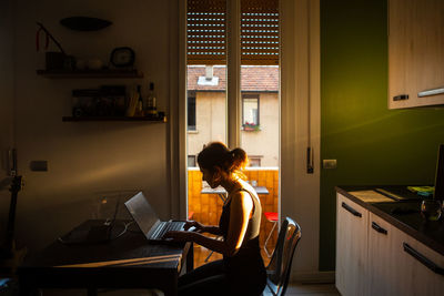 Side view of woman using laptop at home