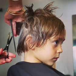 Cropped hand of woman cutting hair of boy