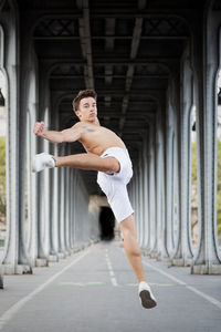 Full length portrait of shirtless young man jumping below bridge