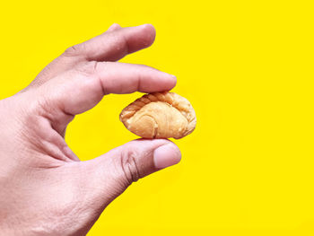 Close-up of hand holding ice cream cone against yellow background