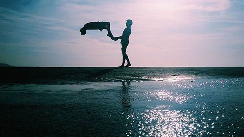 Silhouette of woman jumping in sea at sunset