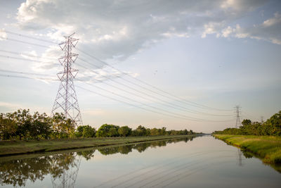 Electricity pylon and trees reflecting on lake