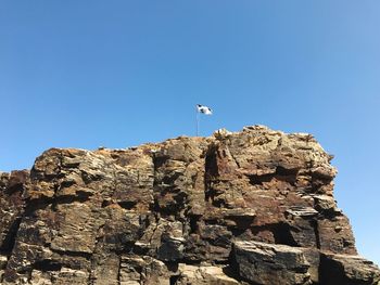 Low angle view of flag on cliff against clear blue sky