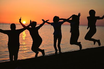 Silhouette people jumping on beach against sky during sunset