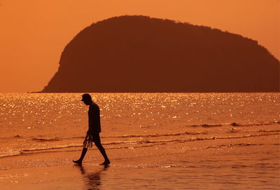 Silhouette man standing on beach against orange sky