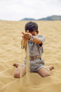 Portrait boy child traveler in a suit of an archaeologist and wearing hat sitting on sand in desert