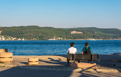 Rear view of people by sea against clear sky