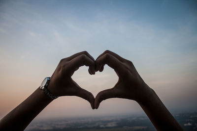 Cropped image of hands making heart shape against cloudy sky