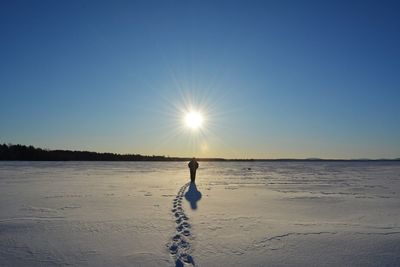 Silhouette person walking on snowcapped landscape against clear blue sky