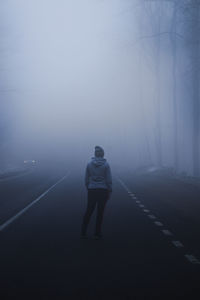 Rear view of woman standing amidst fog on road