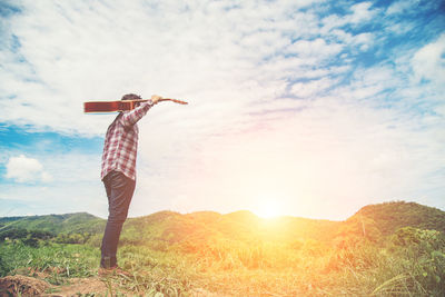 Full length of man holding guitar against sky on field