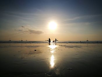 Silhouette people standing on beach against sky during sunset