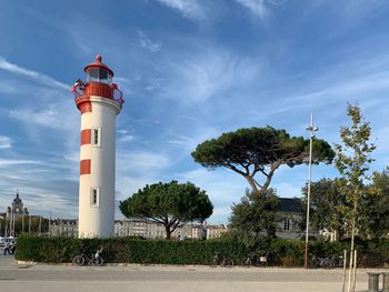 Lighthouse amidst trees and buildings against sky