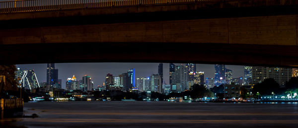 Illuminated city street by buildings against sky at night