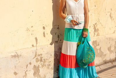 Rear view of woman holding umbrella standing against wall