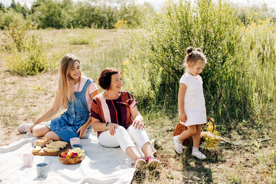 A grandmother and her two granddaughters have a picnic in nature, spend time together on weekends