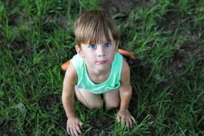 High angle view of portrait boy kneeling on grass outdoors