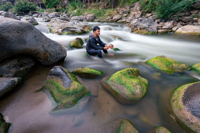 Woman sitting on rock in stream