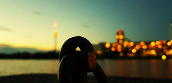 Silhouette man by illuminated chain against sky at sunset