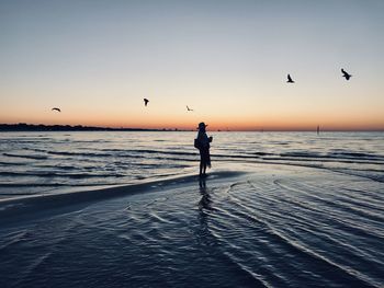 Silhouette woman standing in sea against clear sky during sunset