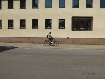 Man riding bicycle on road by building
