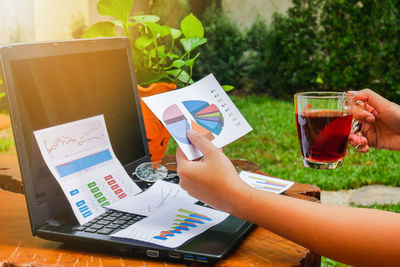 Cropped image of woman holding graph while having black coffee