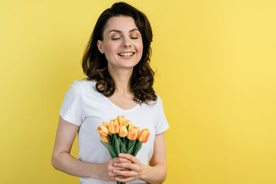 Young woman holding yellow flower against orange background