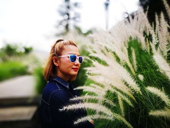 Side view of woman in sunglasses standing by pampas grass at park