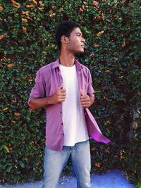 Young man looking away while standing against plants