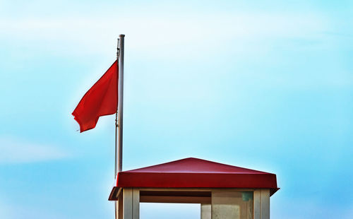 A bright warning flag near a lifeguard tower ,blue and cloudy sky