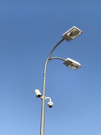 Low angle view of street light and security camera against clear blue sky