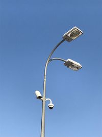 Low angle view of street light and security camera against clear blue sky