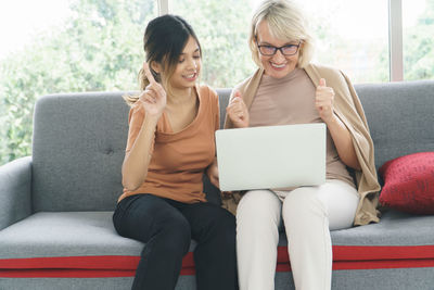 Smiling young woman using mobile phone while sitting on sofa