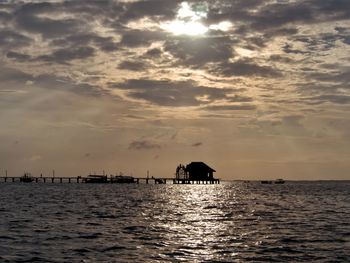 Silhouette hut in sea against sky during sunset
