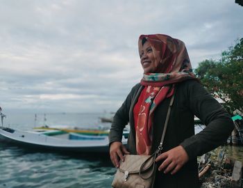 Smiling young woman standing by boat against sky