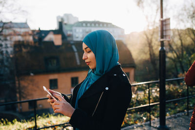 Young muslim woman wearing hijab using smart phone in city