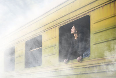 Low angle view of woman peeking through window during foggy weather
