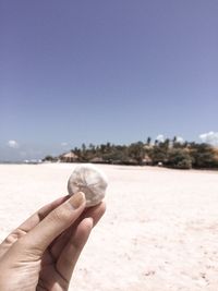 Hand holding sand at beach against clear sky
