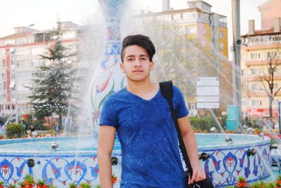 Portrait of young man standing against buildings in city